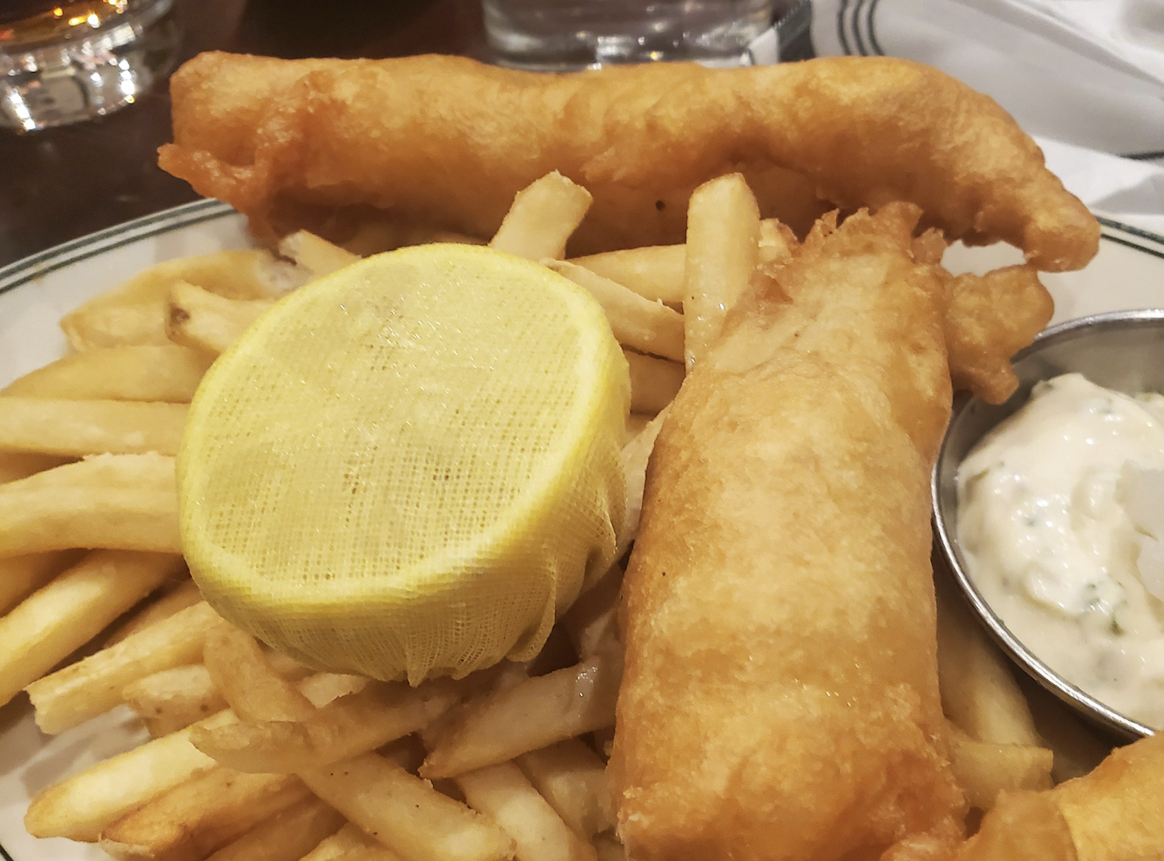 A plate of golden fried fish and French fries is served with a lemon slice and a side of tartar sauce.