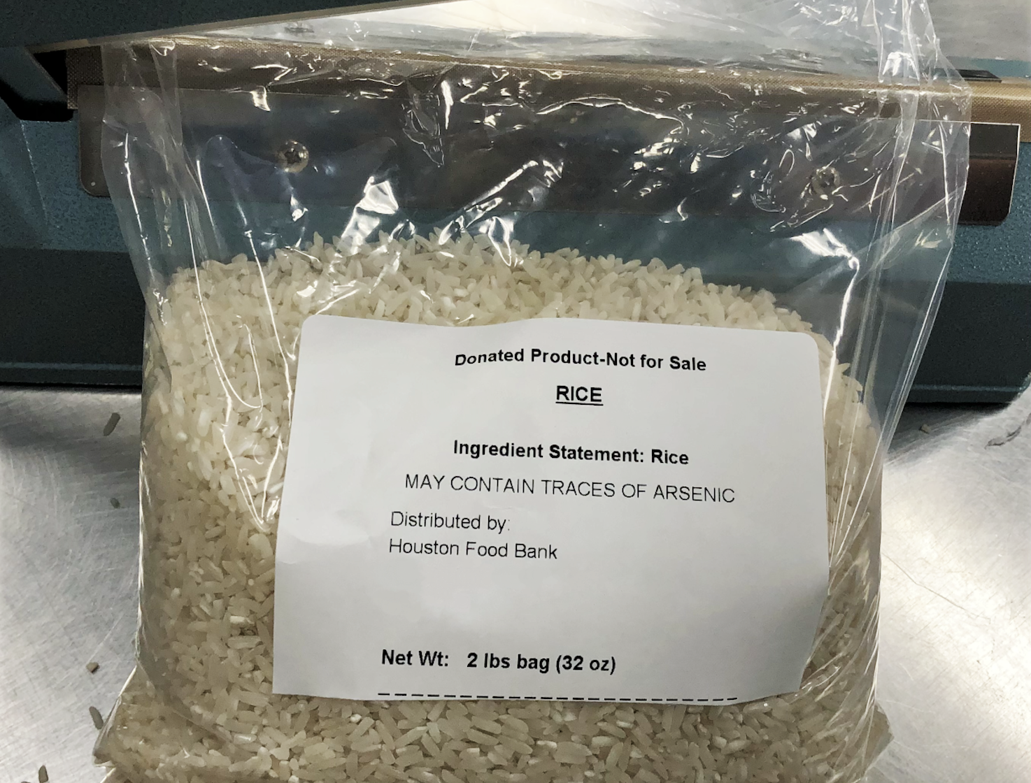 A clear plastic bag of rice with a label stating “Donated Product-Not for Sale,” “Ingredient Statement: Rice,” “May contain traces of arsenic,” and “Distributed by: Houston Food Bank.” Net weight: 2 lbs.