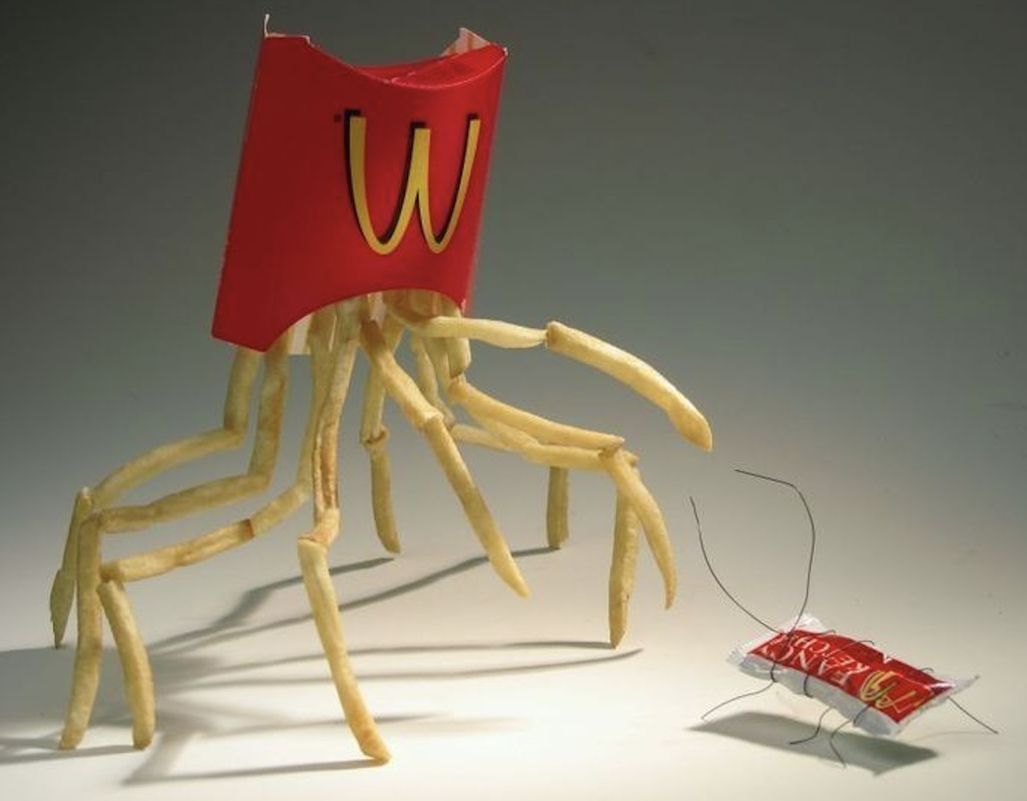 A McDonald’s fries container with fries as legs resembles a crab, approaching a ketchup packet with wire legs that looks like a bug.