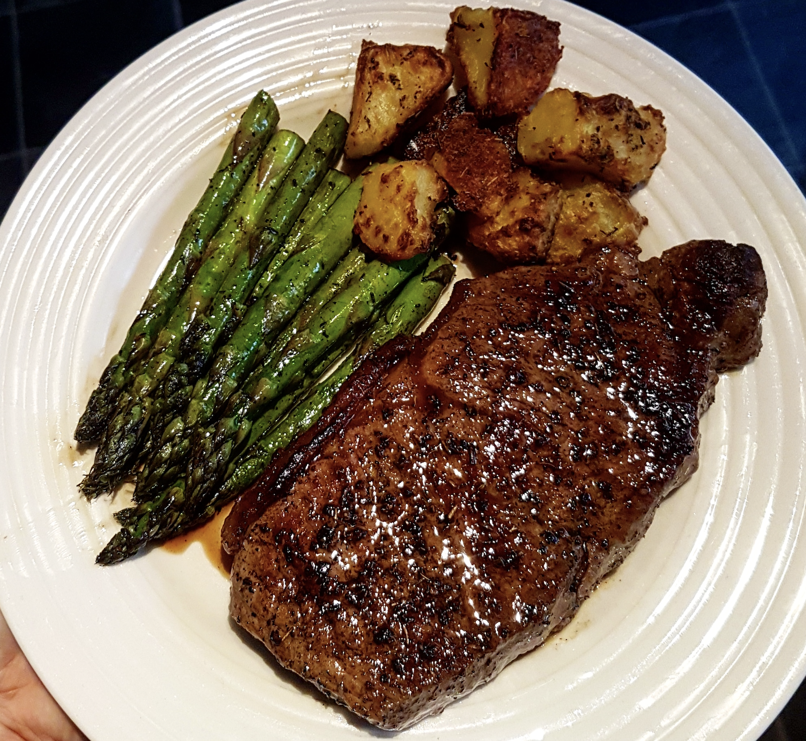 A white plate with grilled steak, roasted potatoes, and seasoned asparagus spears, arranged neatly and served as a meal.