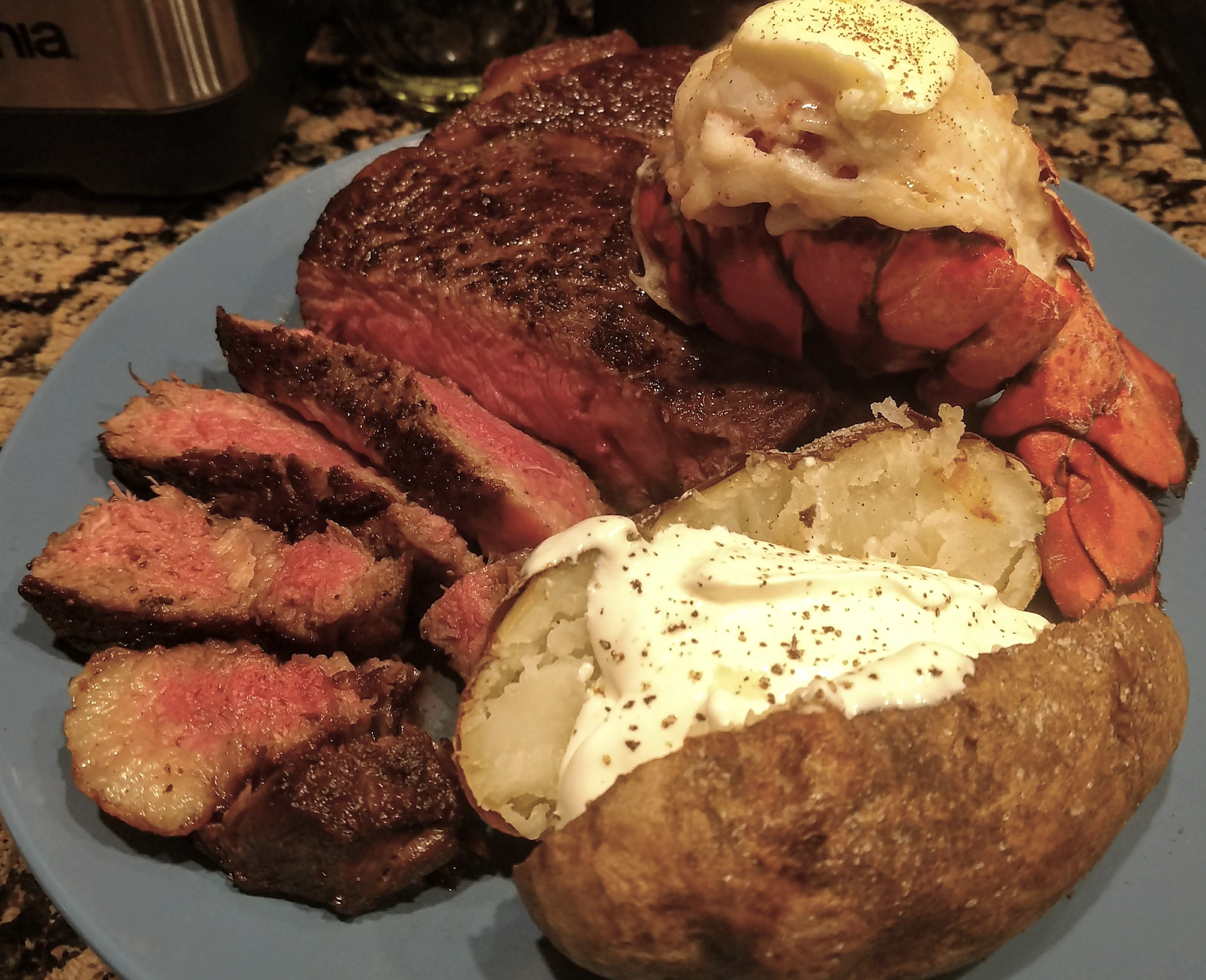 A blue plate with a grilled steak, sliced medium-rare steak, a baked potato topped with sour cream and pepper, and a lobster tail with melted butter on top.