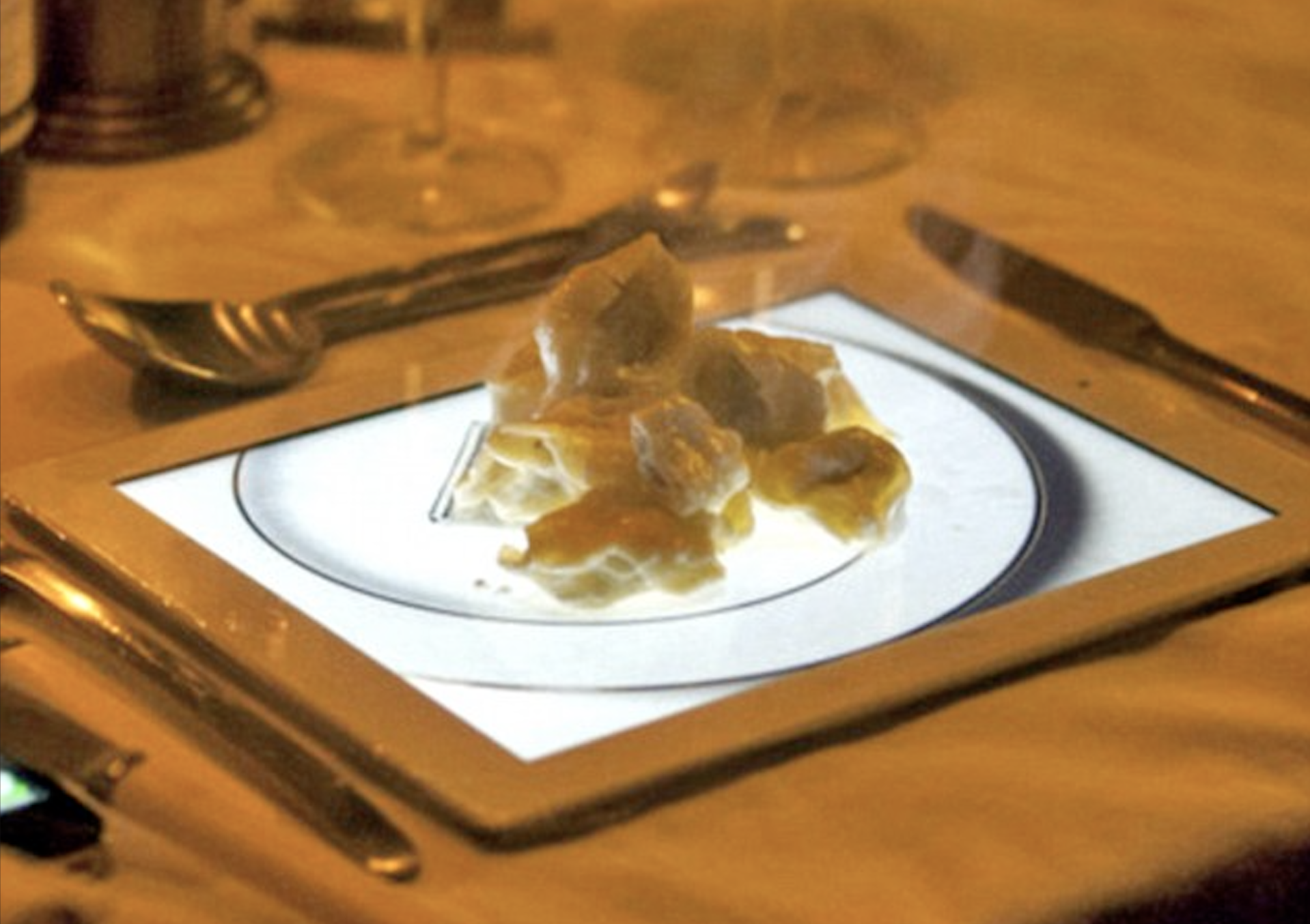 A plate of food is served directly on top of a glowing tablet screen at a restaurant table, surrounded by cutlery and glasses.