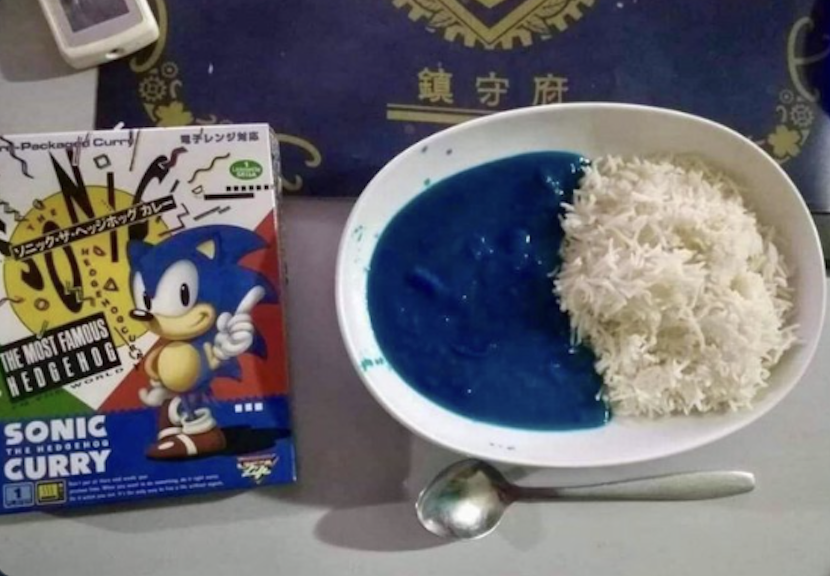Box of Sonic the Hedgehog curry next to a plate with white rice and bright blue curry, and a spoon on the table.