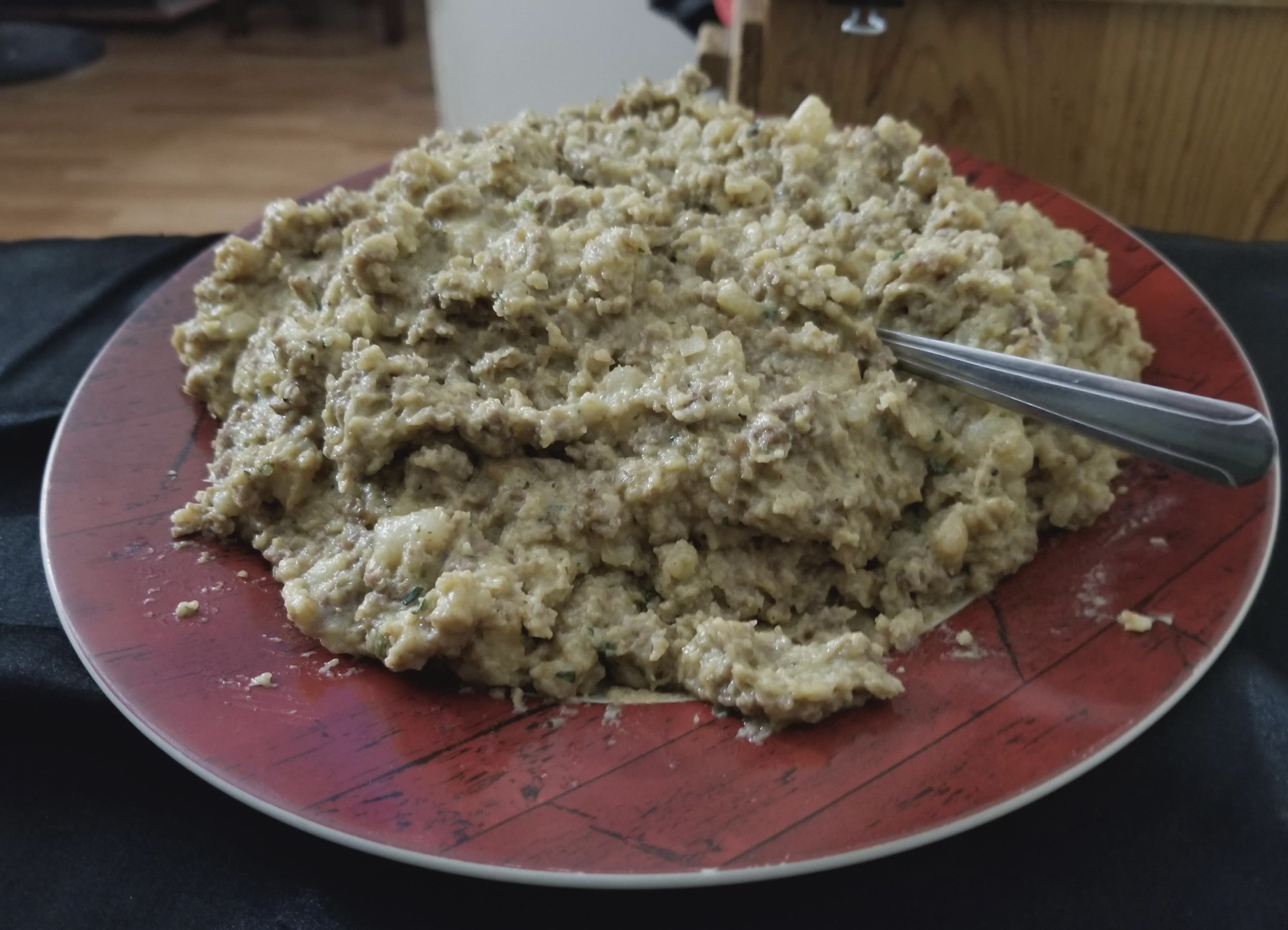 A large serving of homemade stuffing or dressing is piled on a red plate with a spoon resting in it. The dish appears to be moist and chunky, with visible bits of bread and herbs—thankfully, far from any food fails.