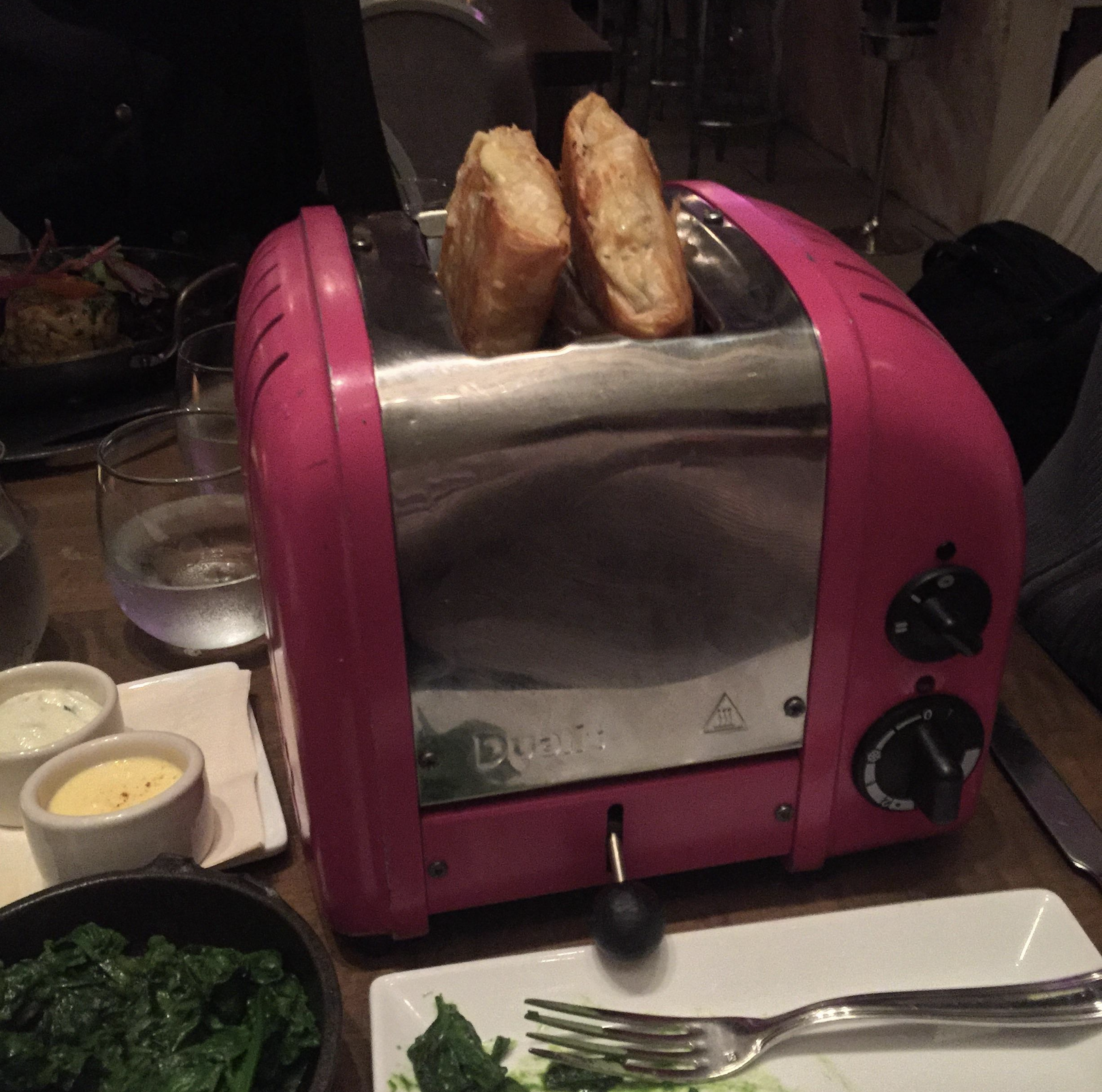 A pink toaster with two pieces of bread is placed on a restaurant table surrounded by dishes and drinks.
