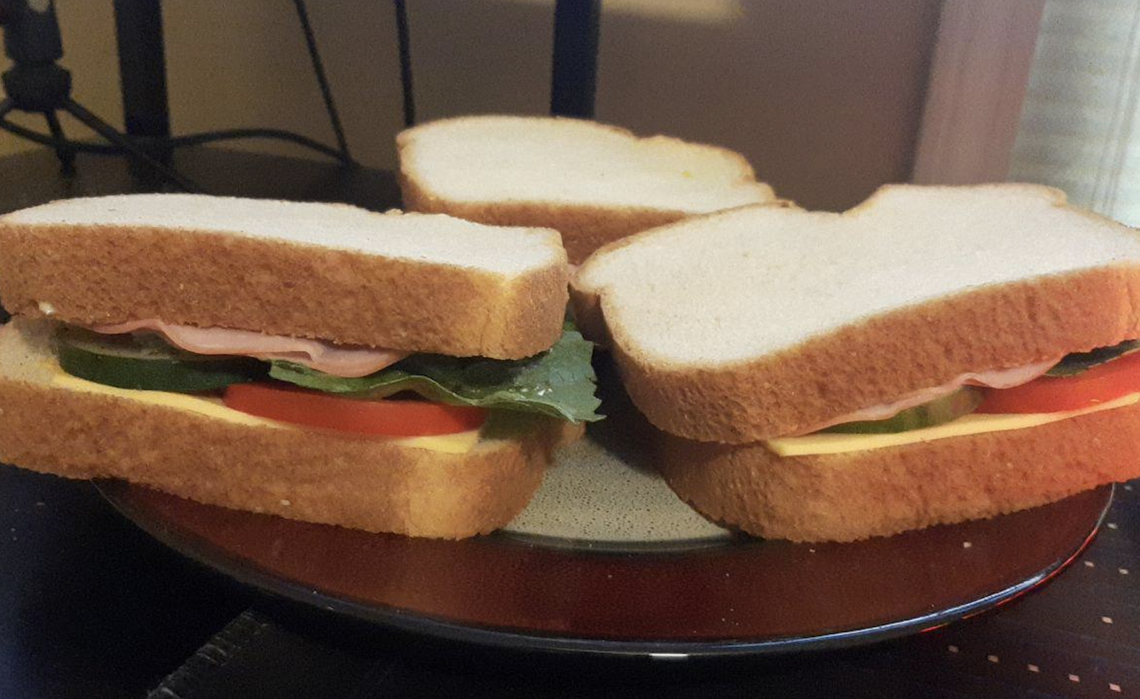 Three sandwiches with white bread, lettuce, cucumber, tomato, cheese, and deli meat are arranged on a plate.