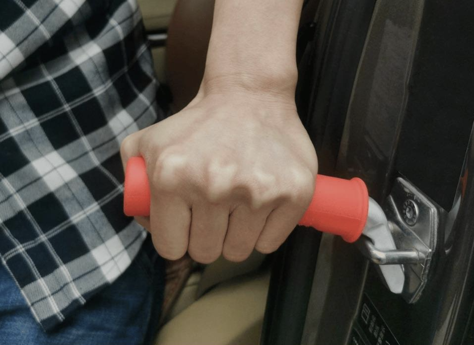 A person gripping a red assist handle attached to a car door latch, likely using it for support while getting in or out of the vehicle.