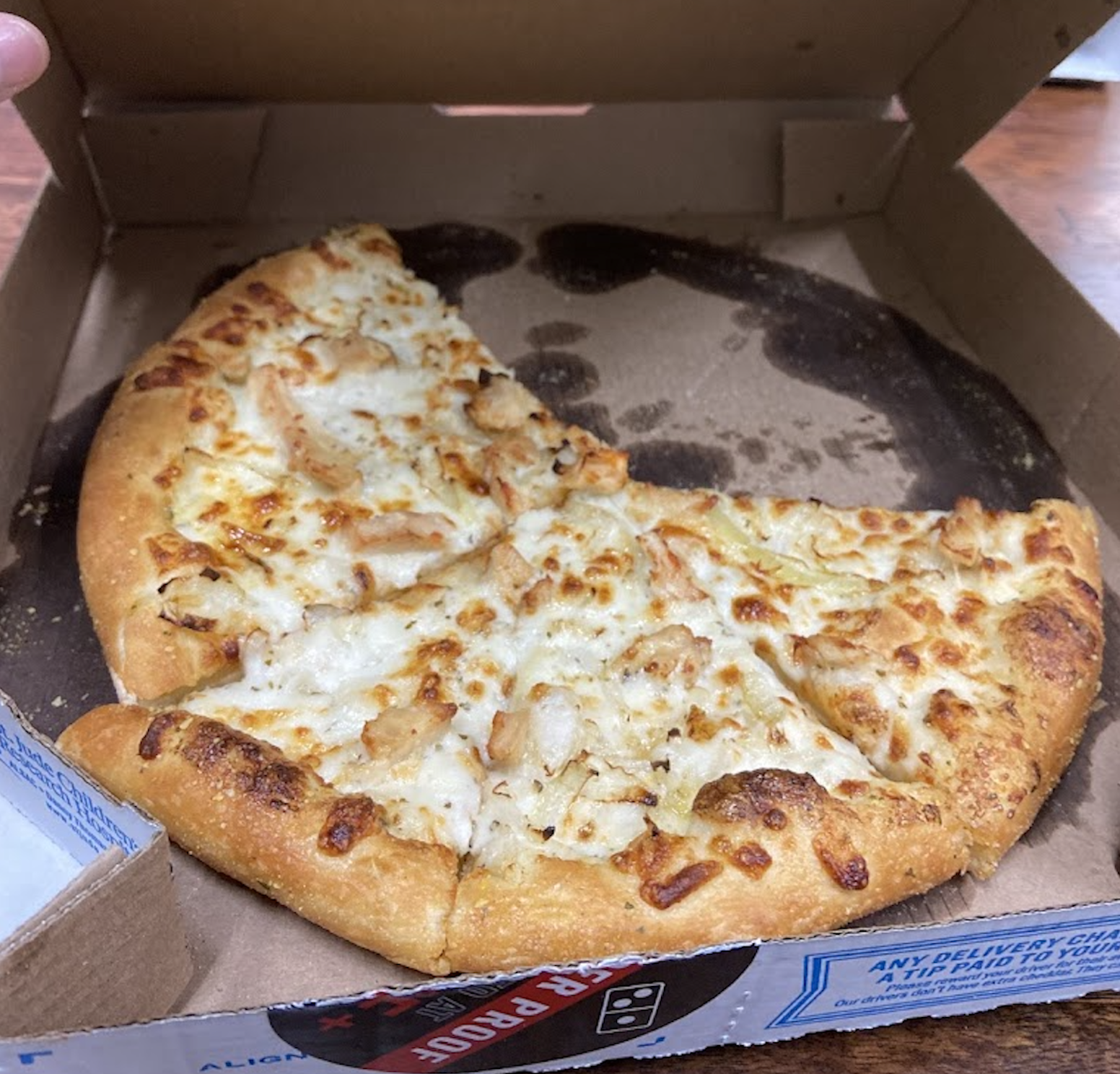An open pizza box with three slices of cheesy chicken pizza left inside. The pizza has a golden crust and is resting on a brown cardboard liner.