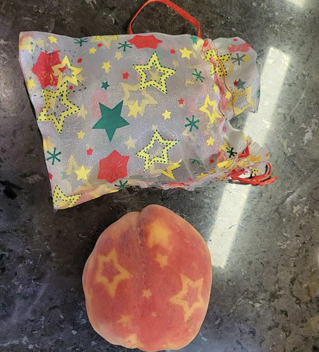 A peach with star-shaped markings sits on a dark surface next to a small drawstring gift bag decorated with colorful stars.