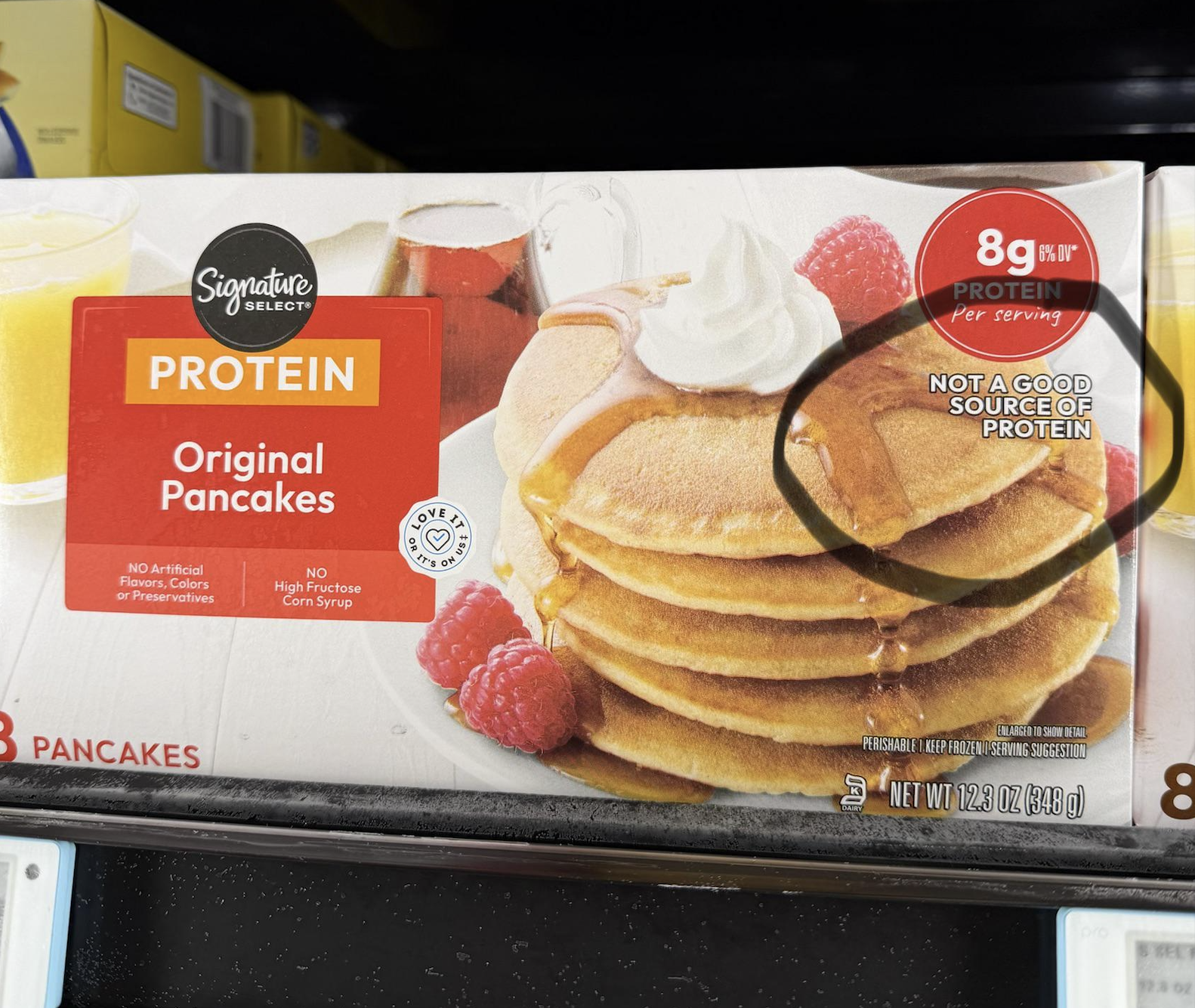 Box of Signature Select Original Pancakes showing pancakes with syrup and fruit. The box claims 8g protein per serving but also says “Not a good source of protein” in a circled area.