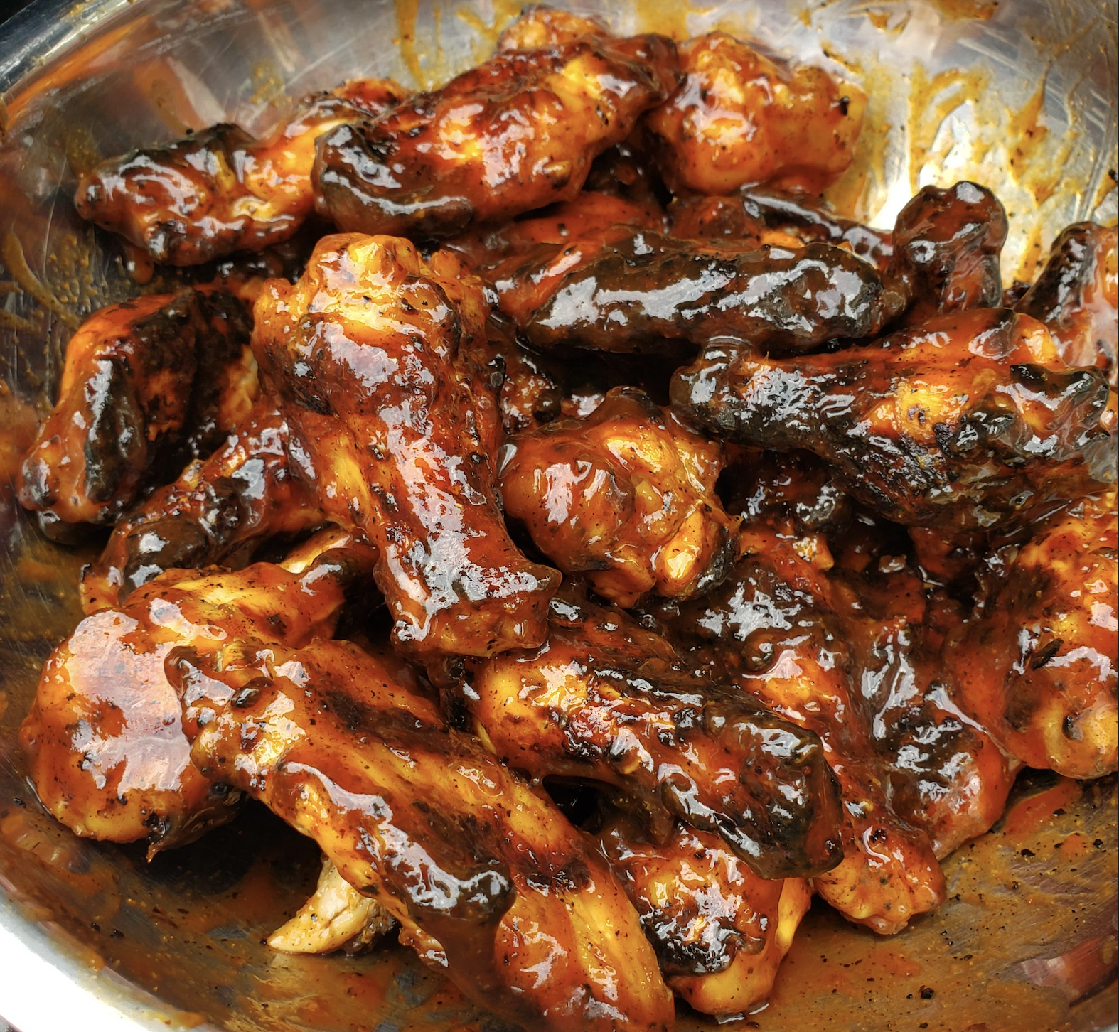 A bowl filled with chicken wings coated in a thick, glossy, dark barbecue sauce. The wings are charred in spots and look sticky and flavorful.