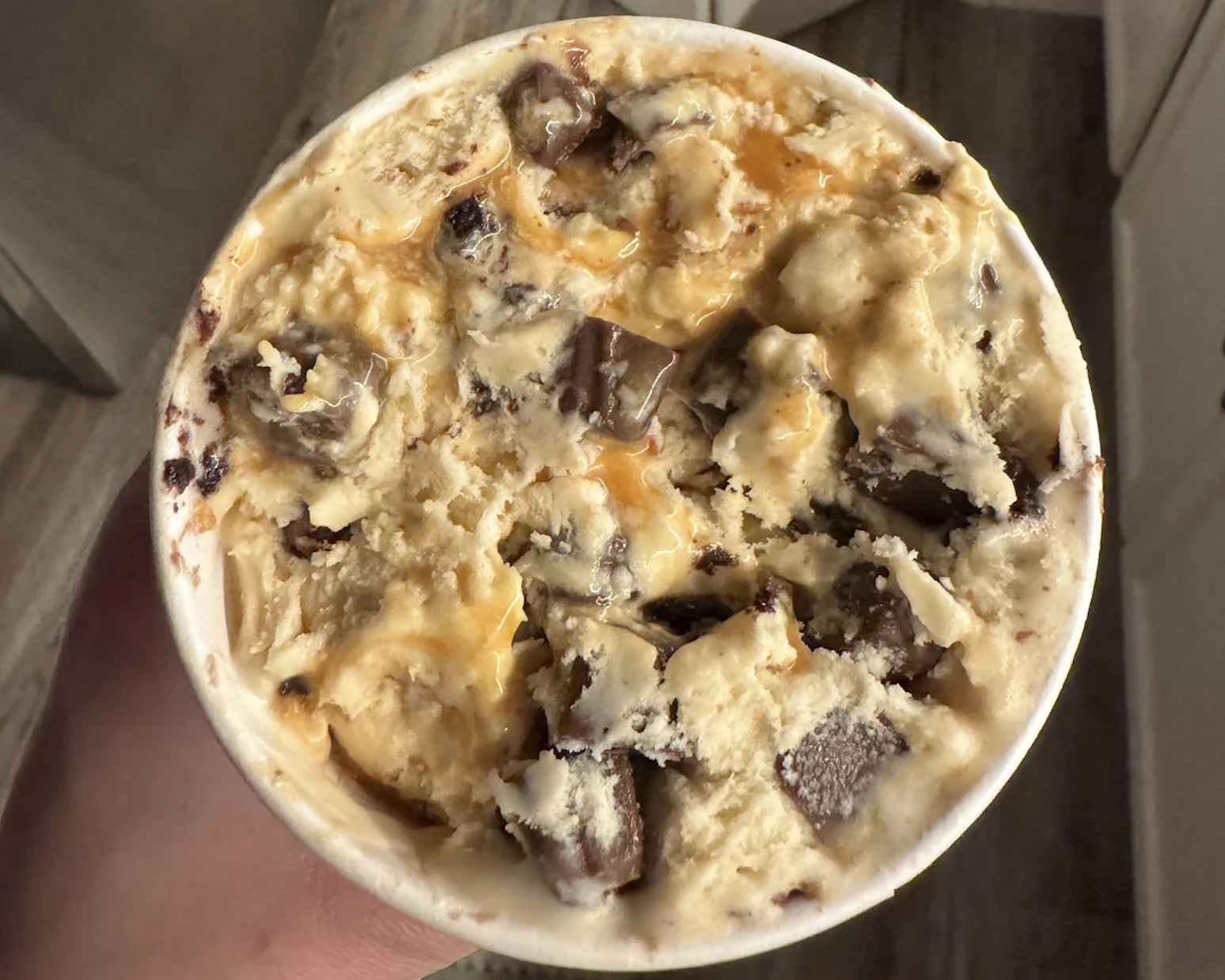 A close-up of a tub of ice cream with caramel swirls and large chocolate chunks mixed into a creamy, vanilla-colored base.