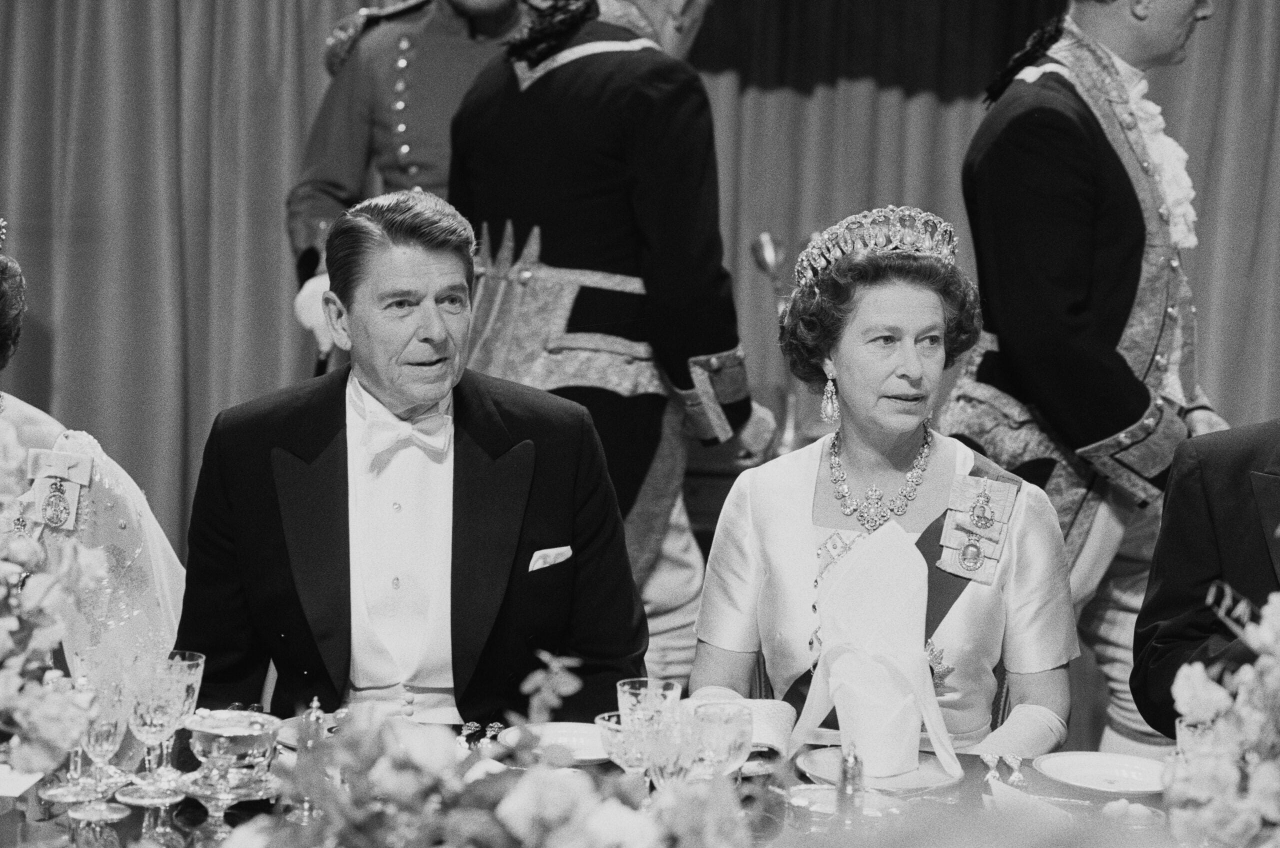 Presidential meals from decades past. A man in a tuxedo and a woman in a gown and tiara sit at a formal dinner table, surrounded by elegantly dressed guests and ornate table settings.