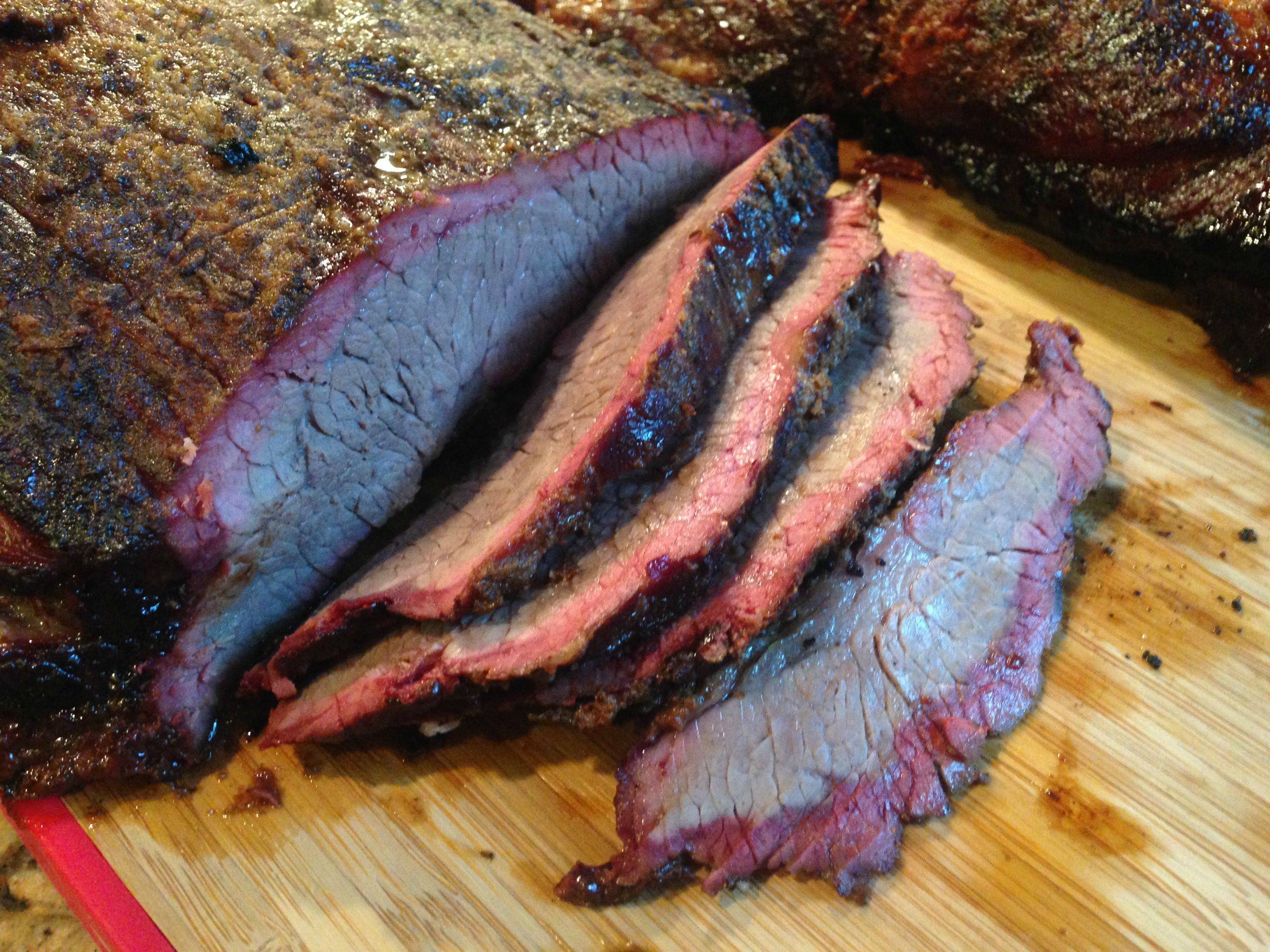 Sliced smoked brisket with a dark, seasoned crust and juicy, tender meat on a wooden cutting board.