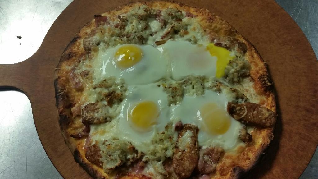 A pizza topped with three sunny-side-up eggs, pieces of sausage, and melted cheese on a wooden pizza board.