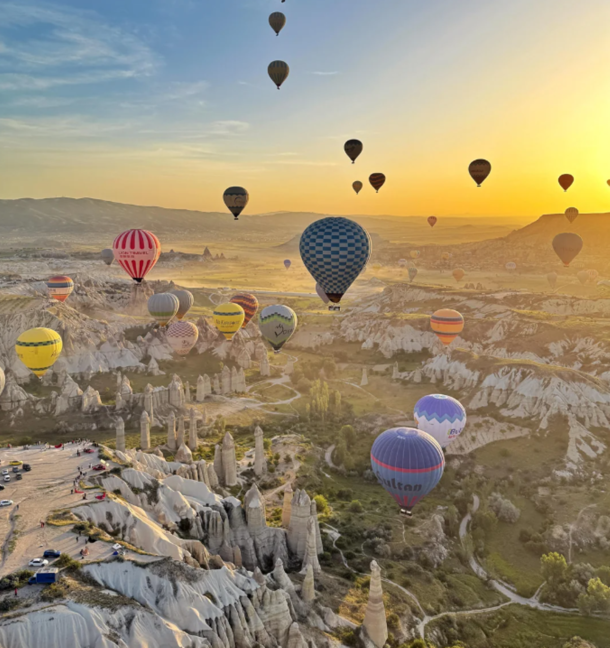 Hot air balloons of various colors float above unique rock formations and green valleys at sunrise, the landscape bathed in warm golden light—a scene reminiscent of travel experiences that went viral for their breathtaking beauty.