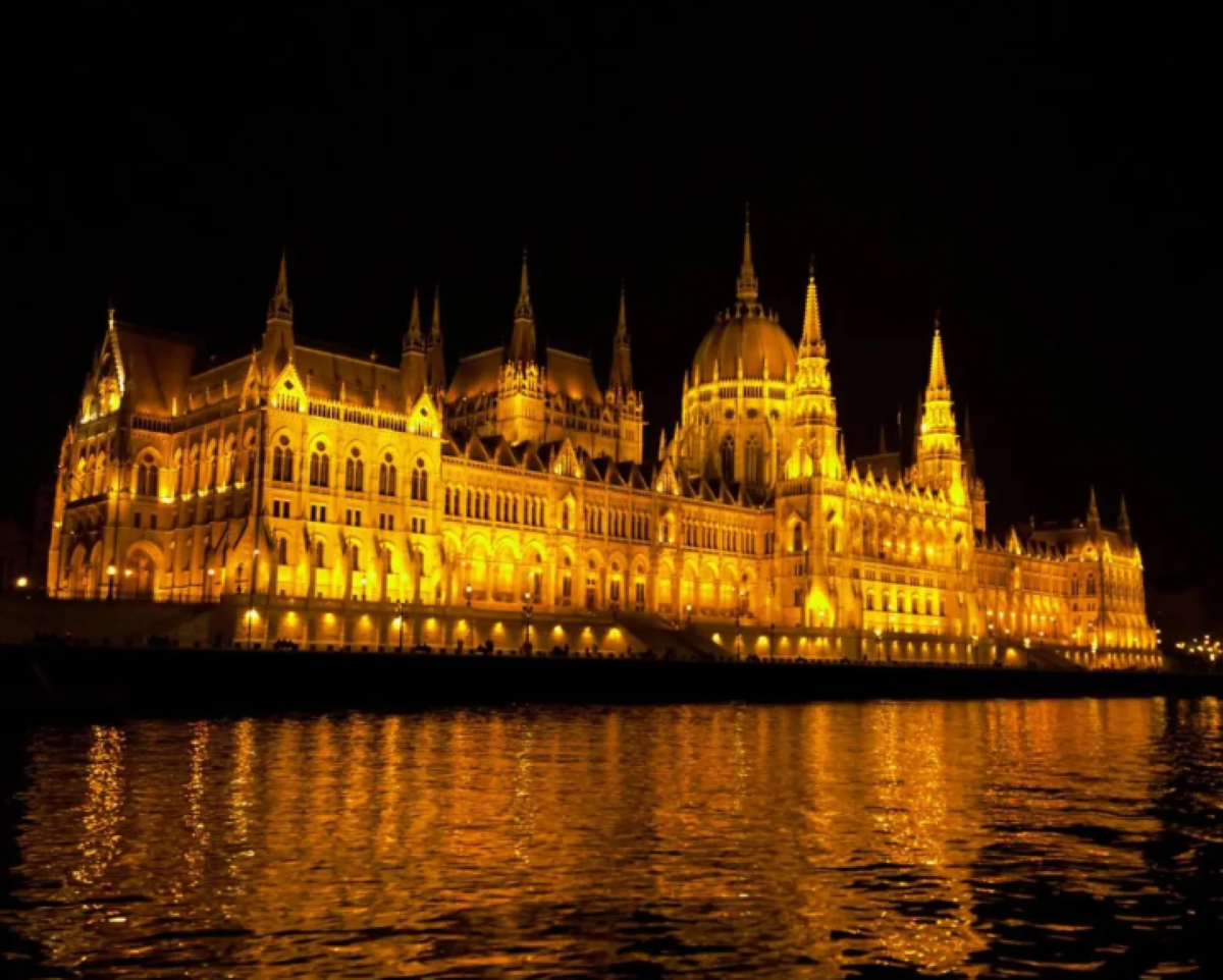 The Hungarian Parliament Building is illuminated at night, with its lights reflecting on the calm waters of the Danube River—a breathtaking sight often featured among travel experiences that went viral.