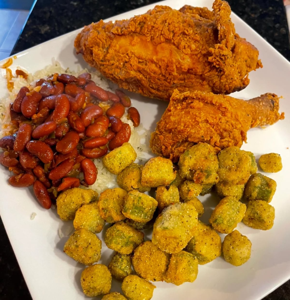 A plate with two pieces of fried chicken, a serving of red beans on rice, and a portion of fried okra arranged on a white square plate.