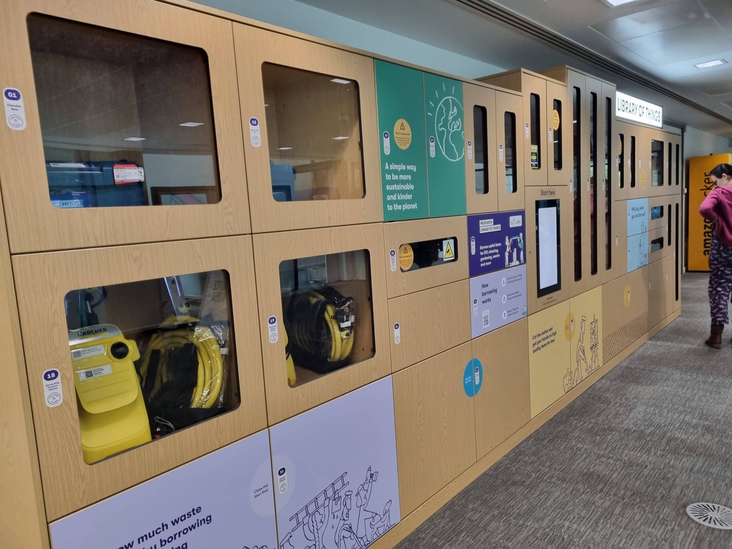 A row of wooden lockers with glass doors, displaying various equipment and informational graphics, in a brightly lit indoor space. A person stands to the right, partially out of frame.