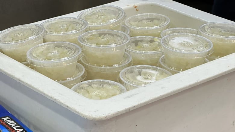 Several clear plastic containers filled with chopped white onions are stacked neatly in a white bin. The containers have lids and are arranged in rows.