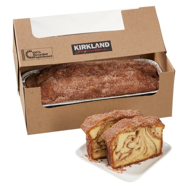 A Kirkland Signature cinnamon loaf in a cardboard box, with two slices on a white plate in front, showing a swirled cinnamon pattern inside the cake.