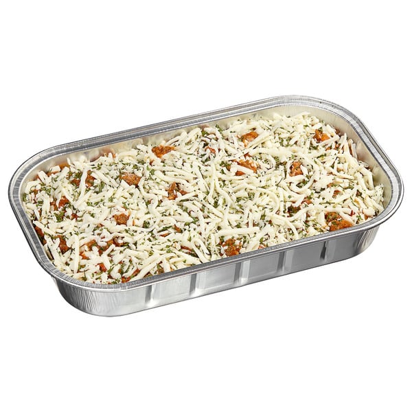 A rectangular foil tray filled with an unbaked dish, topped with shredded cheese and herbs, likely ready to be baked or cooked.