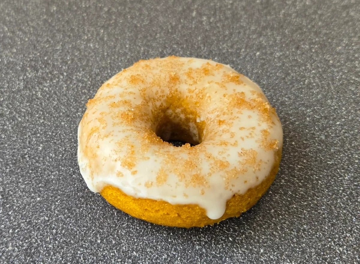 A single pumpkin donut with white glaze and sprinkled brown sugar sits on a gray speckled countertop.