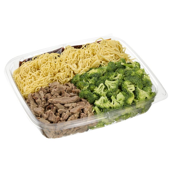 A clear plastic container with cooked noodles, sliced beef, and steamed broccoli arranged in separate sections.