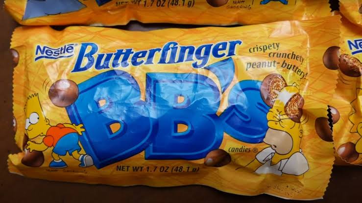 A yellow Butterfinger BB’s candy package featuring Bart and Homer Simpson, with images of chocolate-covered candies and the text “crispey, crunchety, peanut-buttery.”