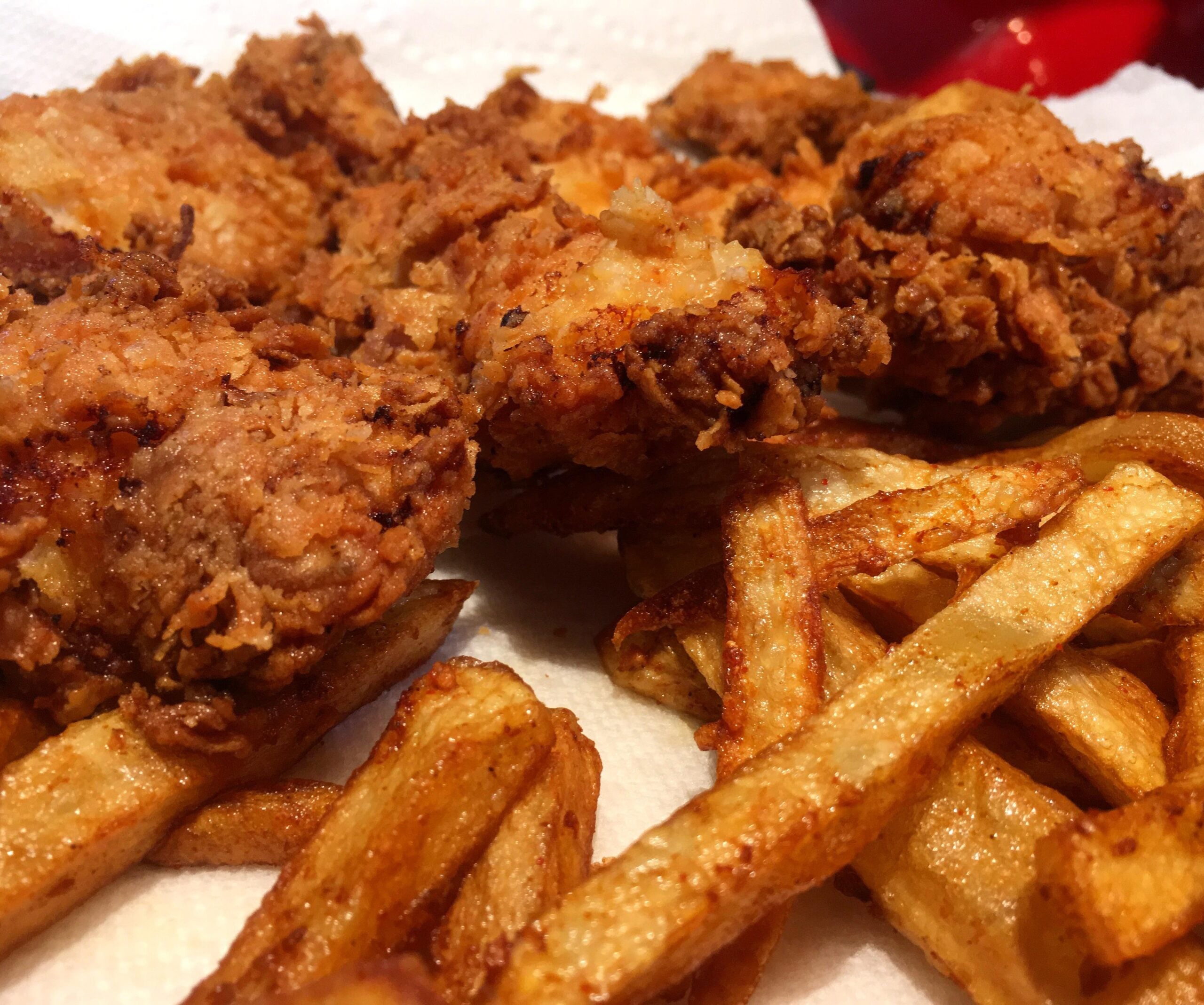 Crispy fried chicken pieces and golden French fries on a white paper towel, with a red object blurred in the background.