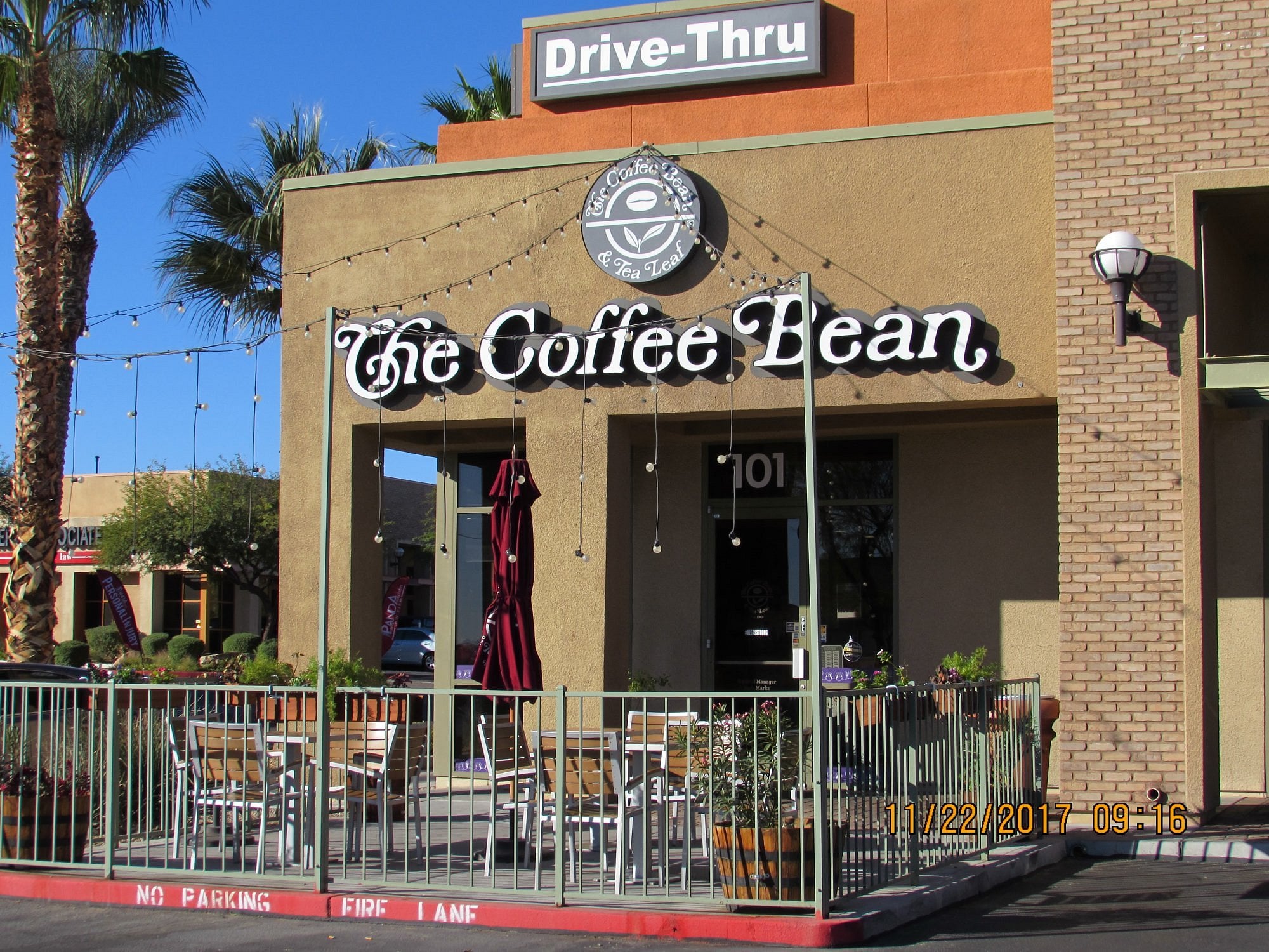 Outdoor seating area of The Coffee Bean café with tables, chairs, string lights, and potted plants. “Drive-Thru” sign above the entrance. Date in photo: 11/22/2017.
