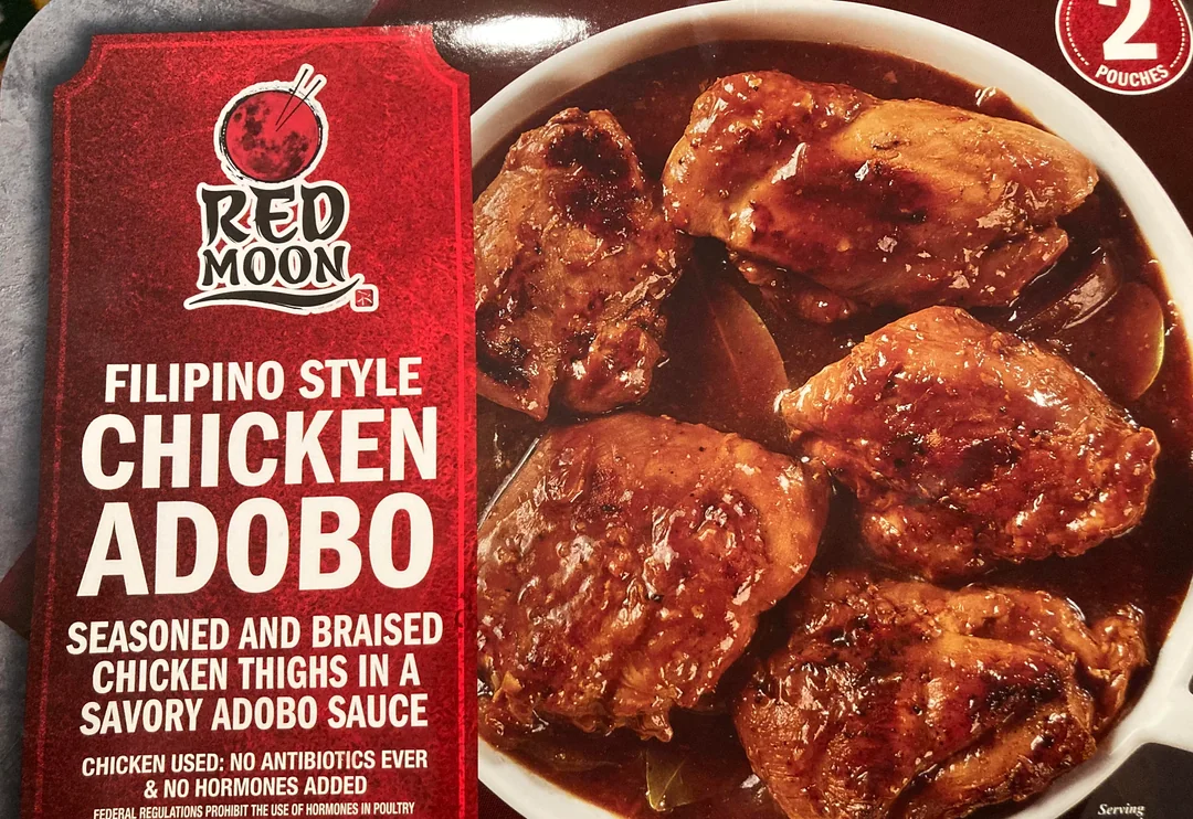 A package of Red Moon Filipino Style Chicken Adobo, showing braised chicken thighs in adobo sauce. The box highlights that the chicken is antibiotic and hormone free, with two pouches included.