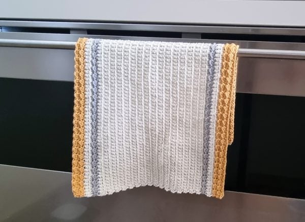 A textured white and gray kitchen towel with yellow edges hangs over a metal oven handle.
