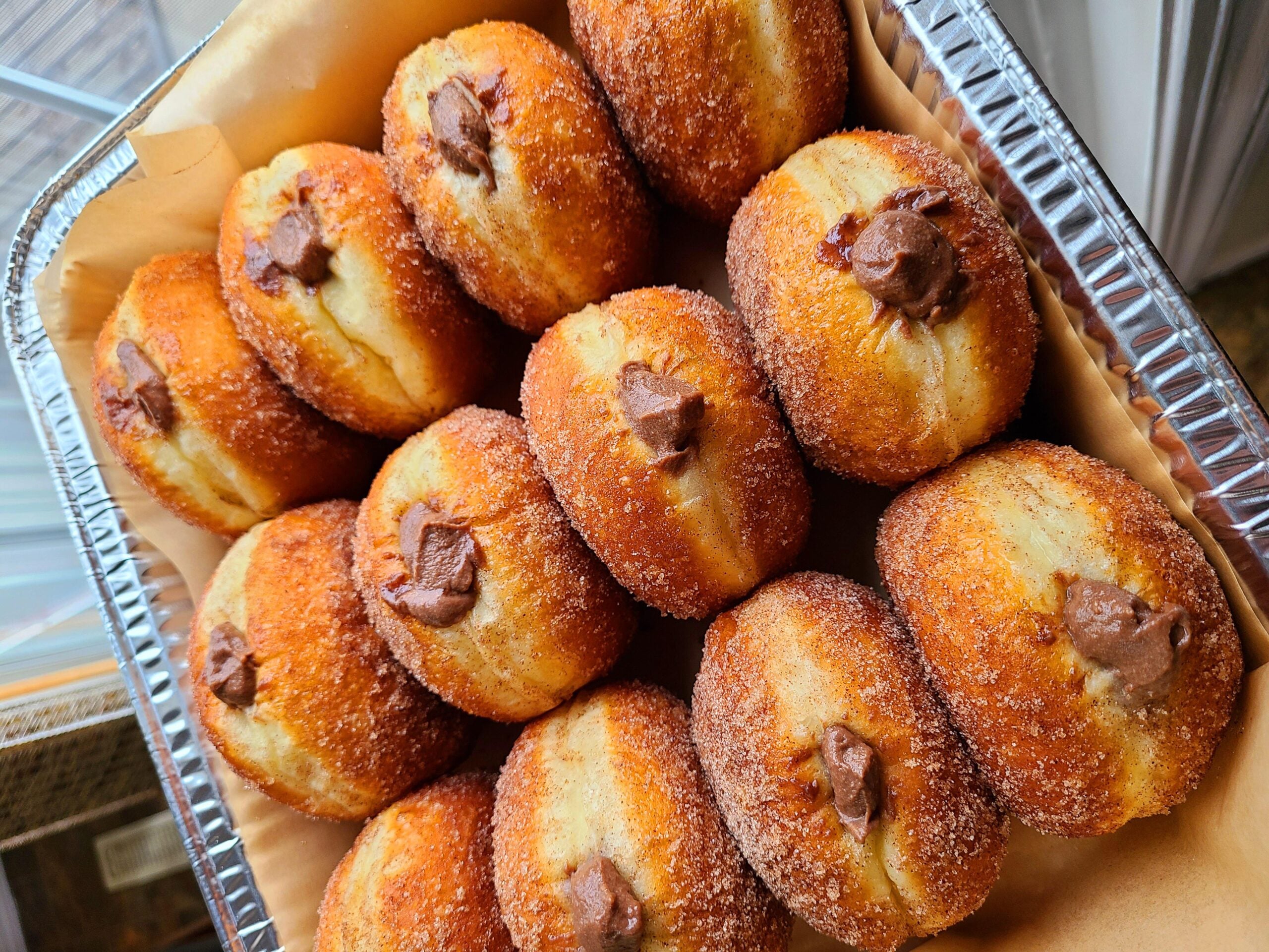 A tray filled with sugar-coated doughnuts, each with a chocolate filling visible in the center, arranged neatly on parchment paper.