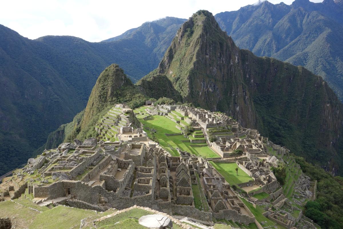 View of Machu Picchu, an ancient Inca city with stone ruins and terraced slopes, surrounded by lush green mountains under a partly cloudy sky.