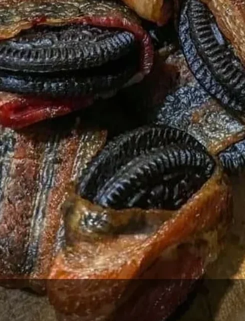 Oreo cookies wrapped in strips of cooked bacon are arranged on a wooden cutting board. Some filling is visible between the cookies, and the bacon appears crispy.