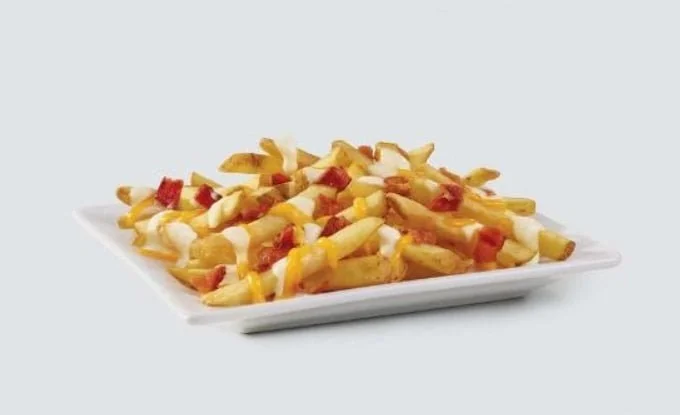A square white plate filled with French fries topped with melted cheese and small pieces of bacon, set against a plain light background.