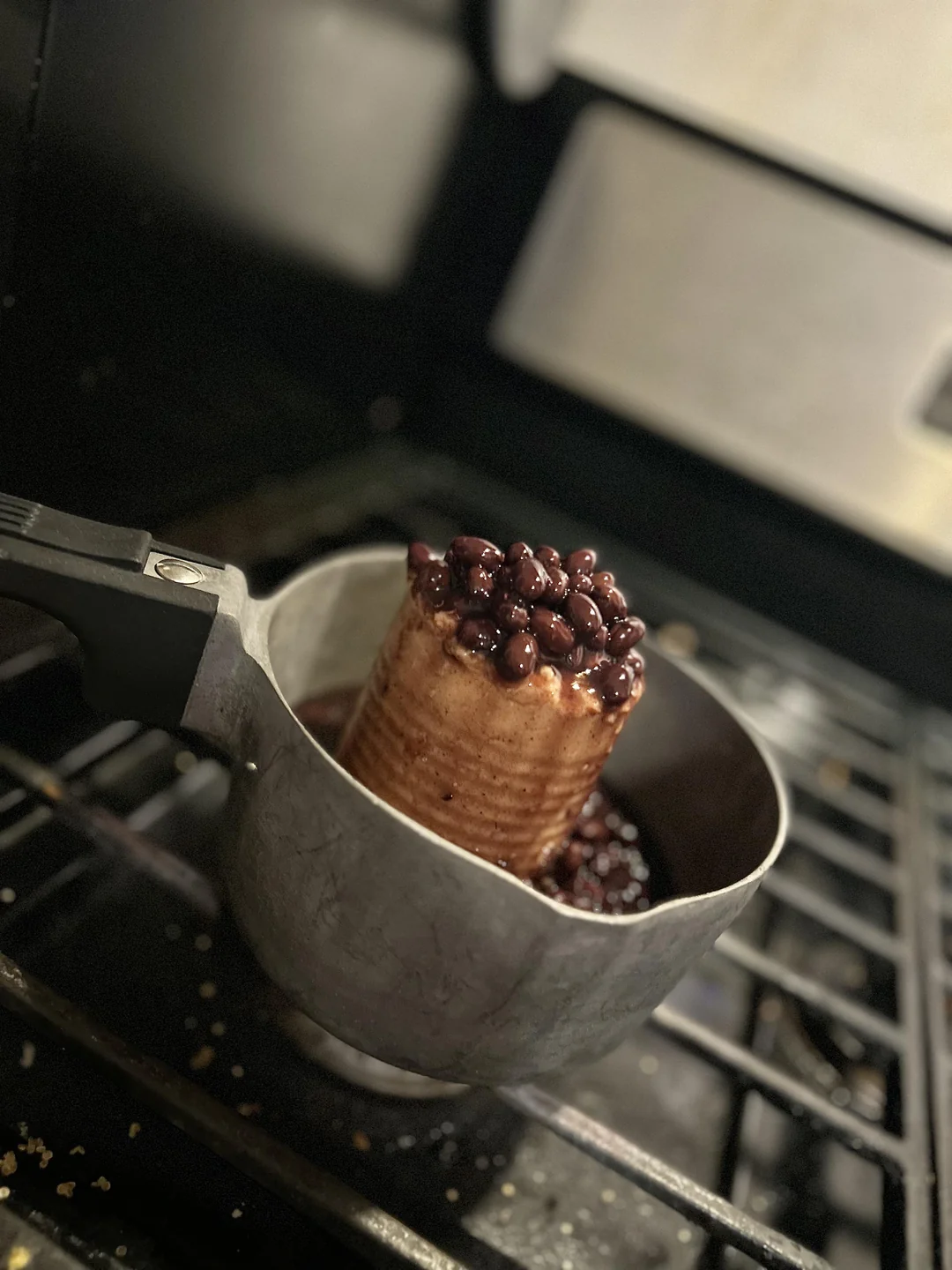 A can of black beans, still in its can shape, sits upright in a pot on a stove with beans spilling over the top. The pot appears to be heating the beans directly from the can. Hilarious food photos.