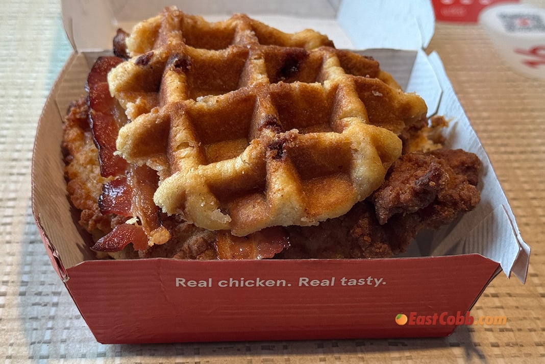 A close-up of a fast-food box containing waffle sandwiches with fried chicken and bacon. The box reads, “Real chicken. Real tasty.” on the side.