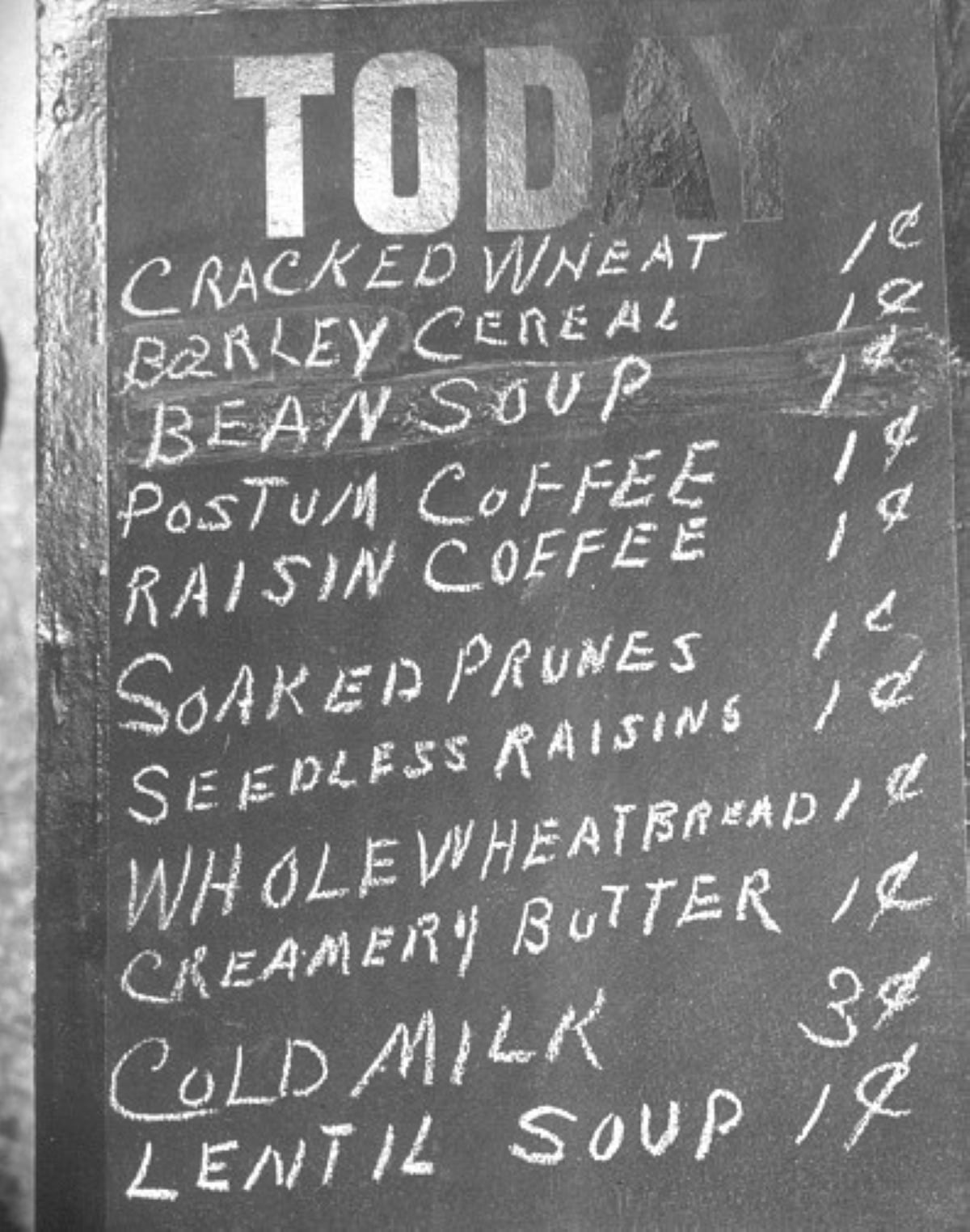 Black and white photo of a chalkboard menu listing meals with historical significance, such as cracked wheat, barley cereal, bean soup, Postum coffee, raisin coffee, prunes, raisins, whole wheat bread, butter, cold milk, and lentil soup.