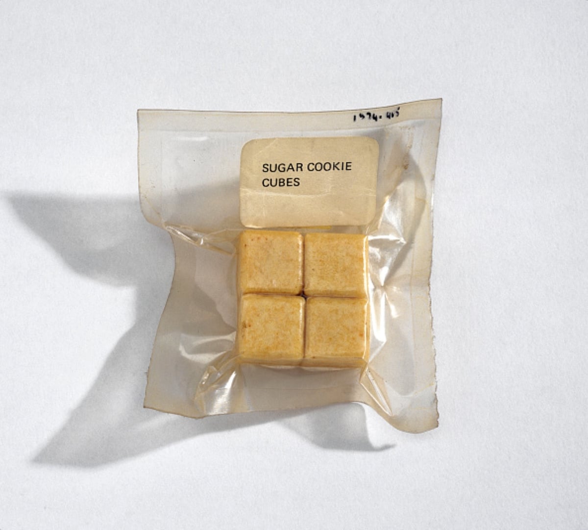 A clear vacuum-sealed packet containing four golden sugar cookie cubes is labeled “Sugar Cookie Cubes.” Reminiscent of meals with historical significance, the packet sits on a plain white background.