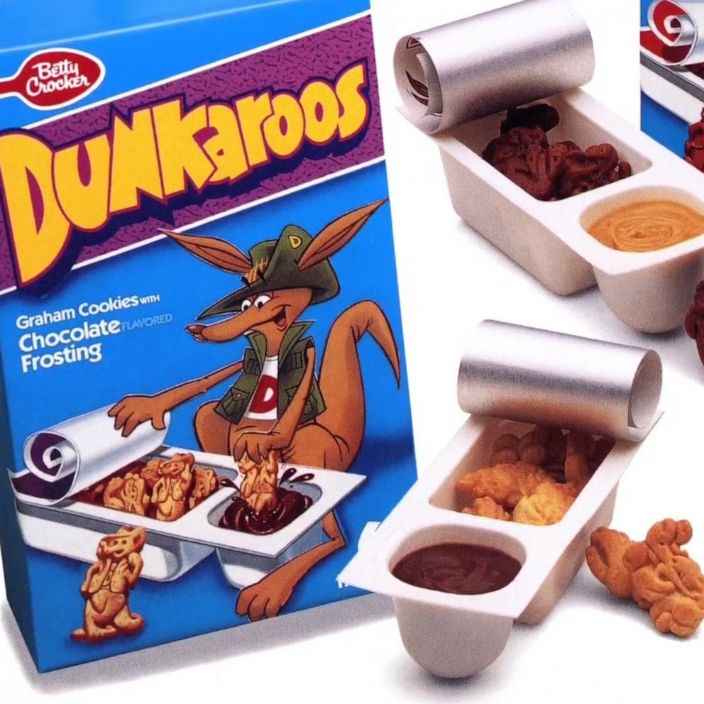 A box of Dunkaroos shows a cartoon kangaroo dipping cookies into chocolate frosting. Open snack trays with cookies and frosting are displayed beside the box.