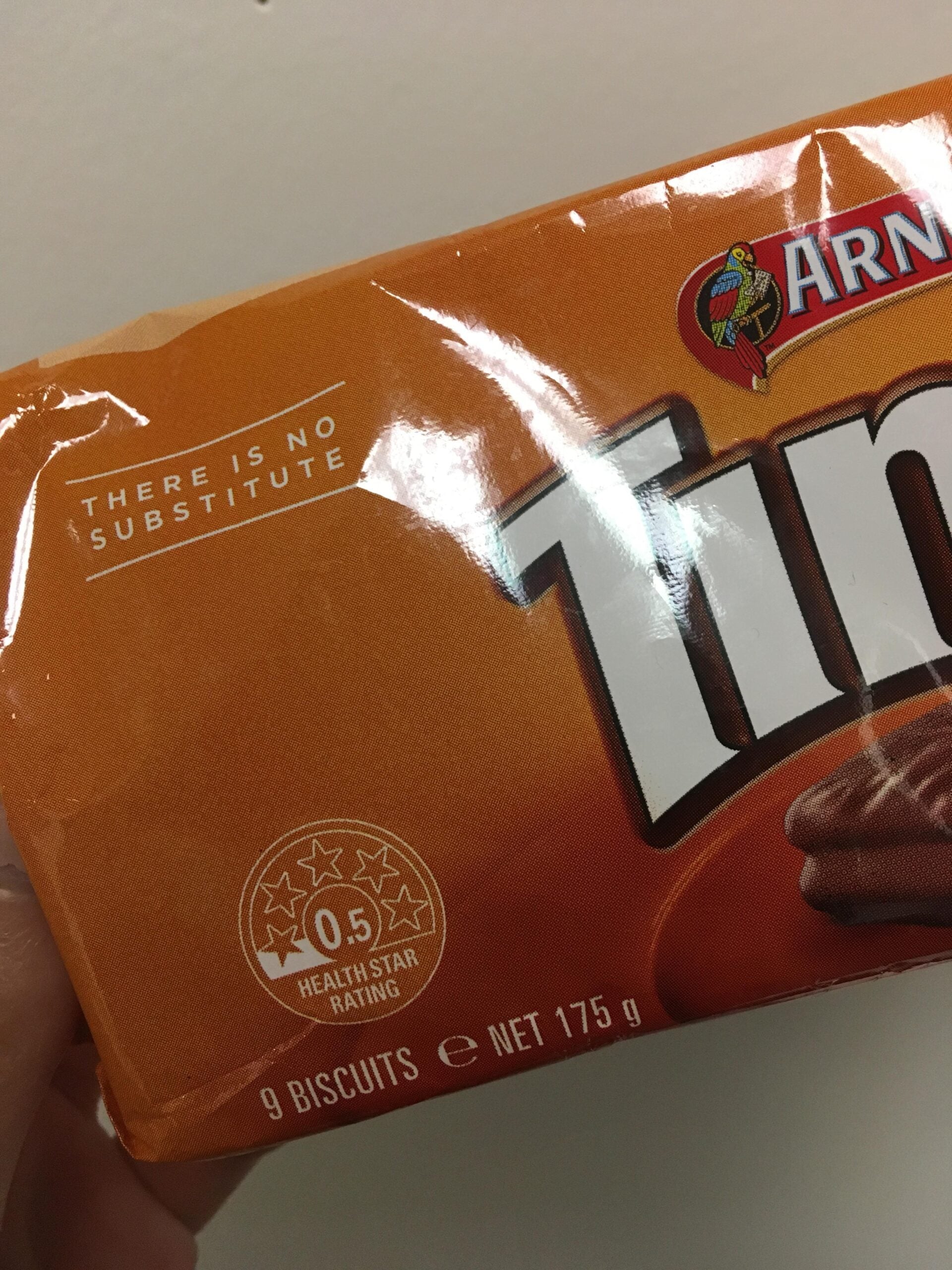 A close-up of an orange Tim Tam biscuit package showing the phrases “THERE IS NO SUBSTITUTE” and “0.5 HEALTH STAR RATING.” The pack contains 9 biscuits, net weight 175g.