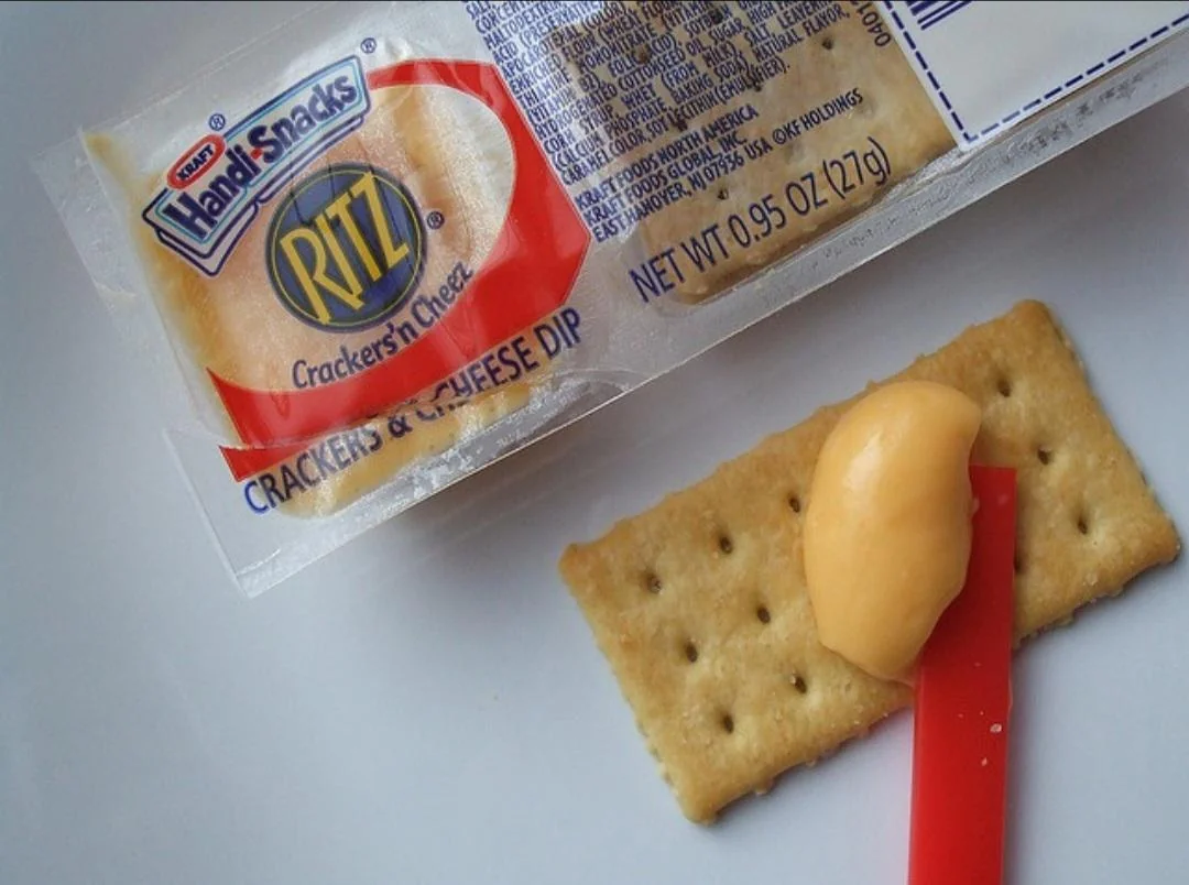 Ritz Handi-Snacks pack with a rectangular cracker, a dab of processed cheese, and a small red plastic spreader on a white surface.