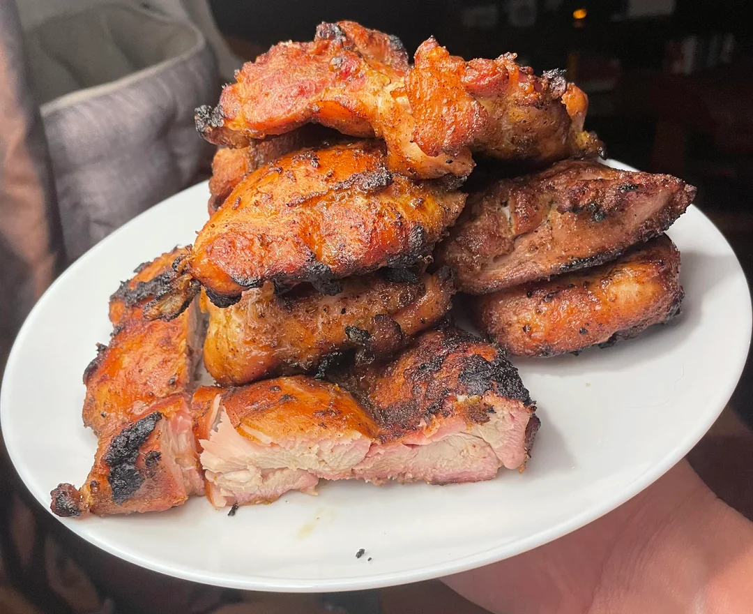 A white plate holds a stack of grilled, charred pieces of seasoned meat, with a few pieces cut to show the juicy, tender inside.