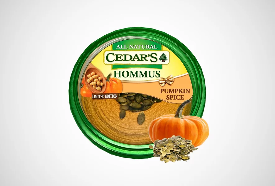 A container of Cedar’s All Natural Pumpkin Spice Hommus is shown with pumpkin seeds and a small pumpkin in front. The label indicates it’s a limited edition flavor.
