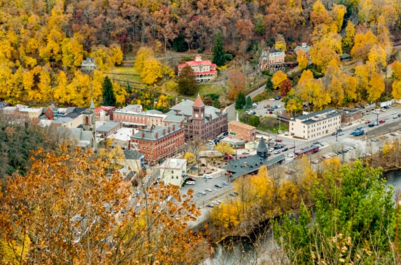 Aerial view of one of the best fall towns in America, surrounded by colorful autumn trees, showing historic brick buildings, houses, parked cars, and winding roads.