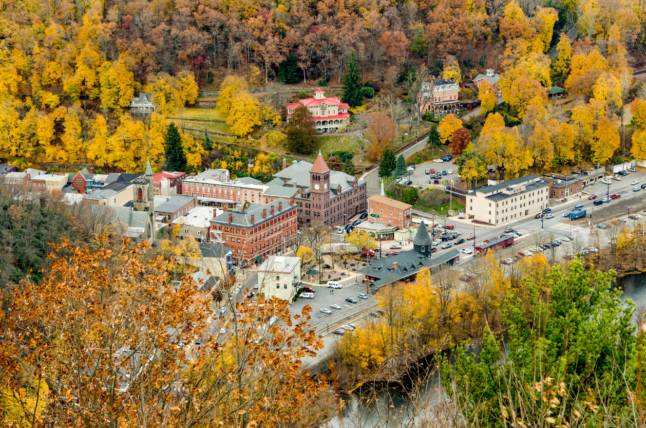 Aerial view of one of the best fall towns in America, surrounded by colorful autumn trees, showing historic brick buildings, houses, parked cars, and winding roads.