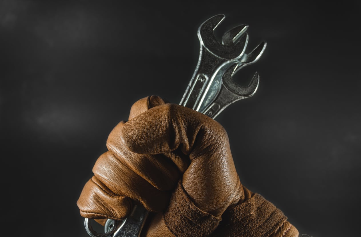 A gloved hand tightly grips two metal wrenches against a dark background, symbolizing strength and labor.