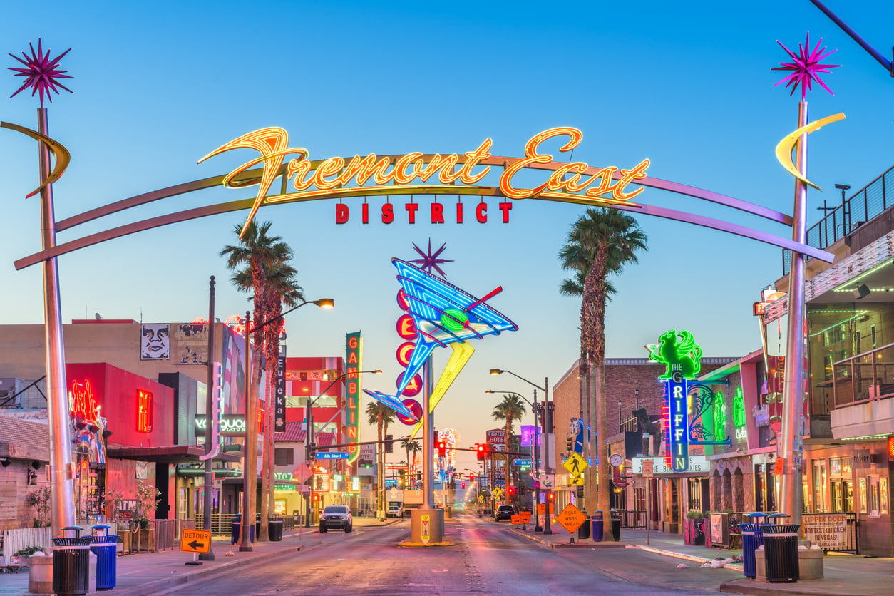 Colorful neon signs light up the entrance to the Fremont East District in Las Vegas at dusk, with palm trees, shops, and bars lining the street under a clear sky—a vibrant scene that perfectly captures some of the most iconic facts about Las Vegas.